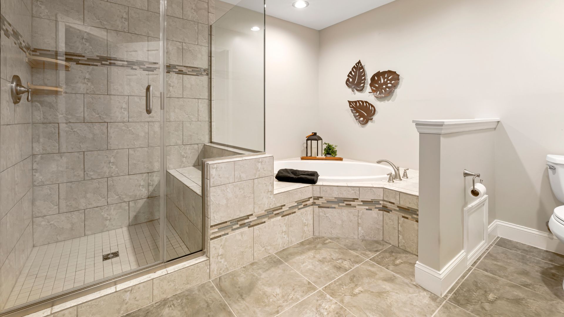 Modern bathroom with glass shower, tiled bathtub, and leaf wall decor