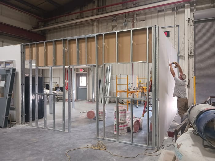 Construction worker installing metal stud wall framing in industrial building