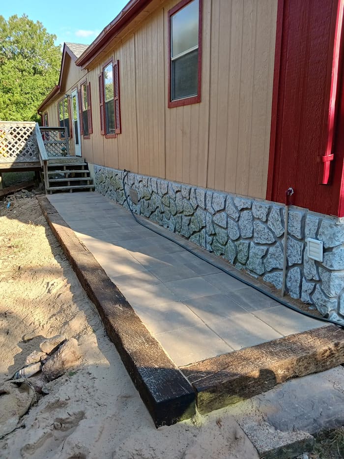 Stone-lined walkway next to mobile home with wooden steps and red trim