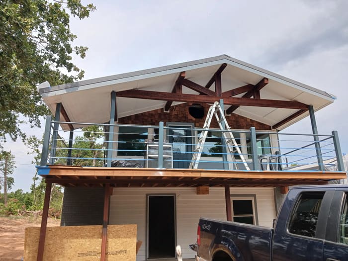 Two-story house under construction with wooden beams and metal railing