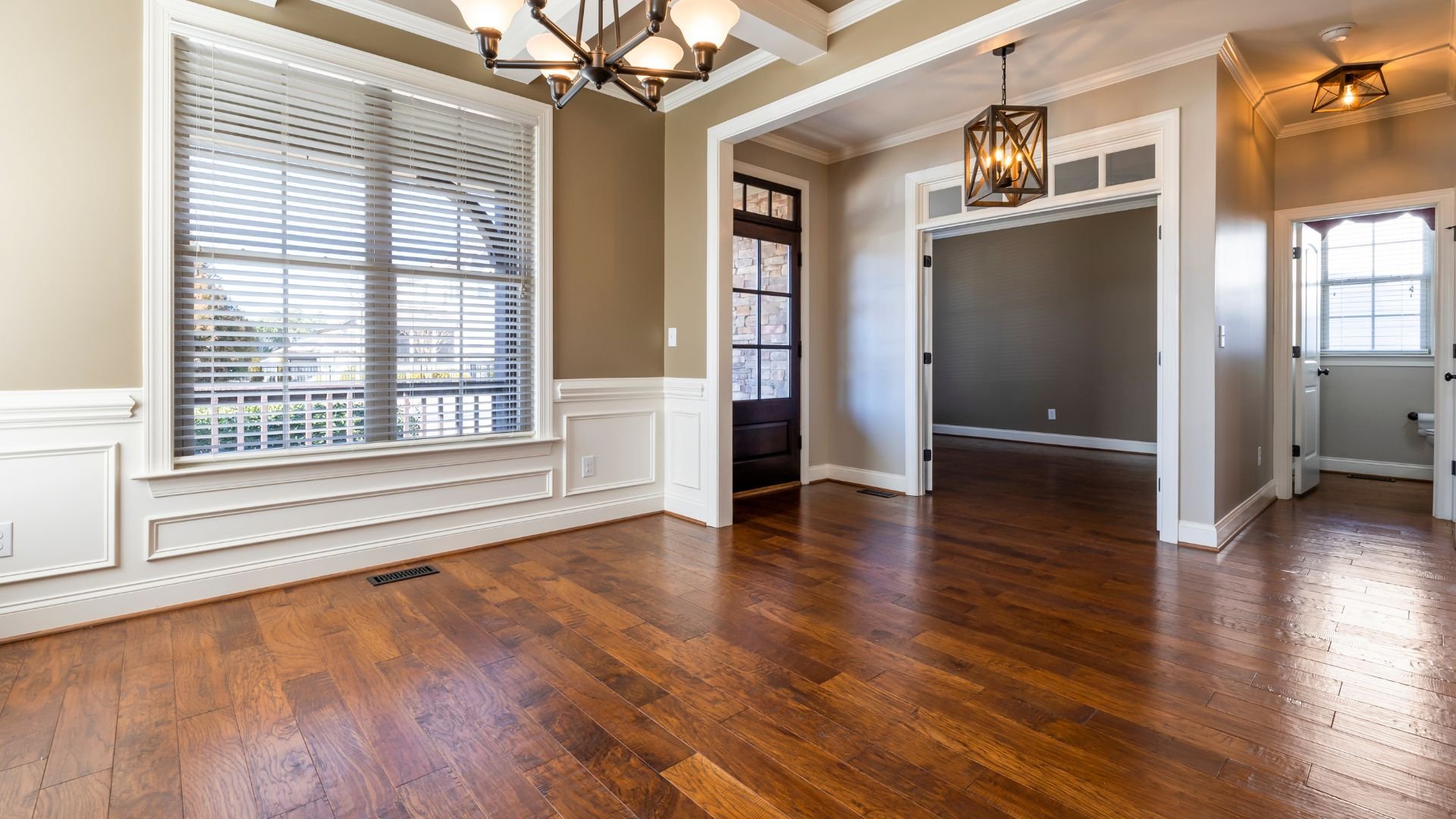 Empty room with hardwood floors, white trim, and elegant light fixtures